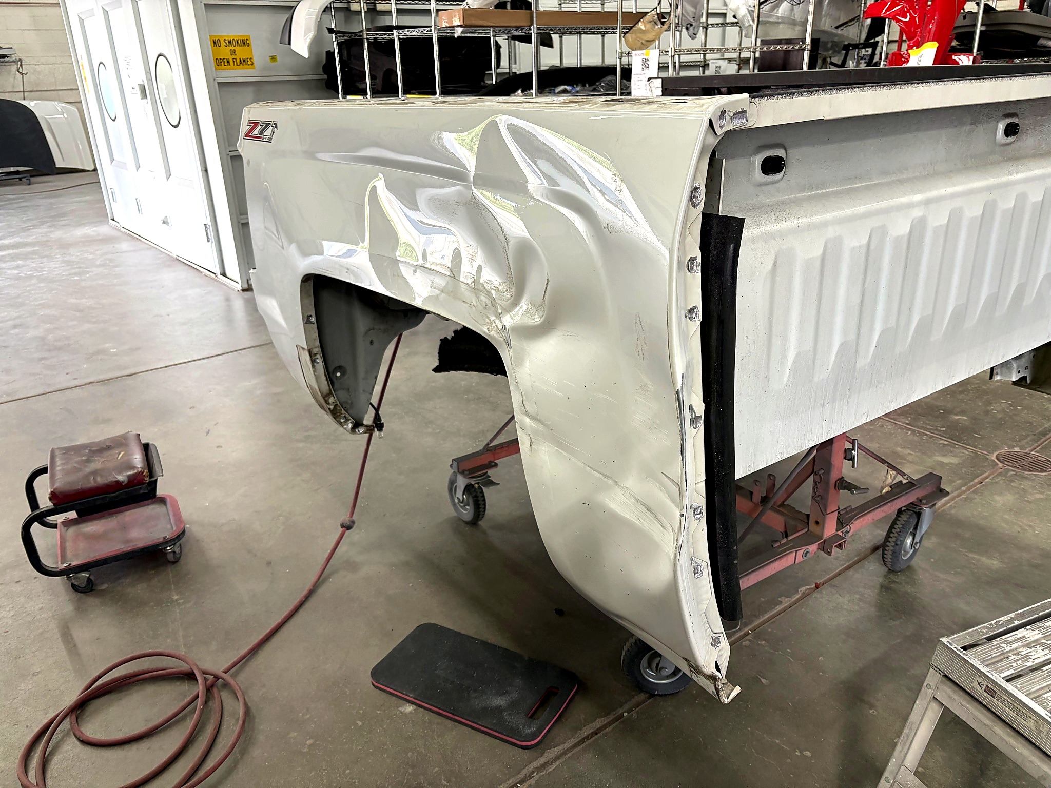 Damaged white truck bed side panel in shop